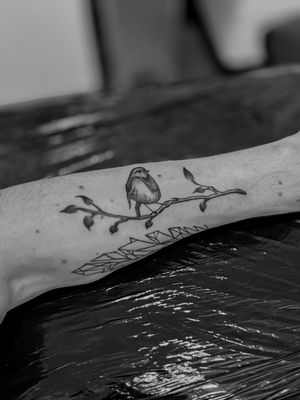 Elegant black and gray illustrative tattoo of a bird perched on a delicate branch, by talented artist Oliver Soames.