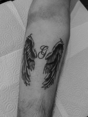 Express your angelic side with this small lettering tattoo featuring wings and your initial, beautifully done by Oliver Soames.