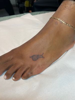Get a unique illustrative tattoo featuring a snail on dark skin, expertly done by tattoo artist Emma InkBaby.