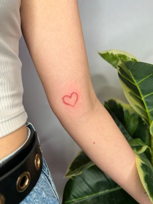 Get inked by Emma InkBaby with a minimalist red heart tattoo in fine line style. Perfect for a subtle and elegant look.