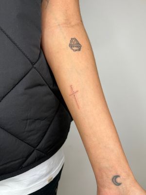 Get a beautifully minimalistic cross tattoo with delicate small lettering done by the talented artist Emma InkBaby.