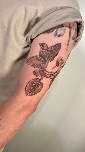 Elegant black and gray tattoo by Sam featuring a beautiful sparrow perched on a delicate flower plant.