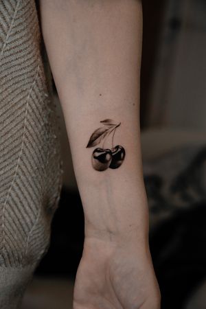 Elegant micro realism cherry tattoo by Viola, showcasing intricate details of a cherry and stem in black and gray ink.