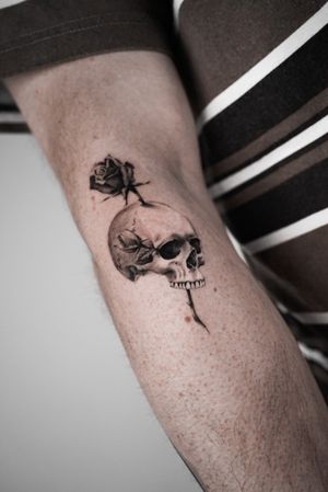 Experience the intricate beauty of this black and gray micro realism tattoo featuring a skull intertwined with delicate roses, expertly executed by the talented artist Viola.
