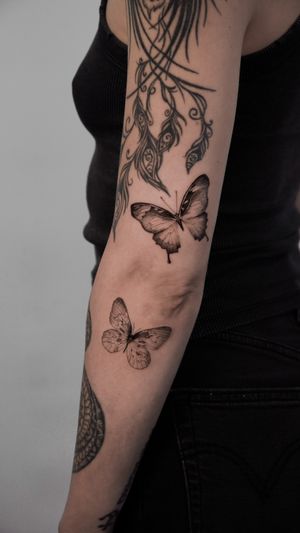 Experience the delicate elegance of a micro realism black and gray butterfly tattoo by artist Viola.