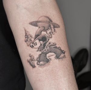 Experience the magic of Disney with a black and gray illustrative tattoo featuring Mickey Mouse as a cowboy exploring Saturn's rings. By Ry Roger.