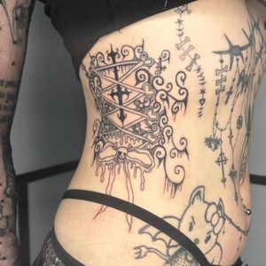 Get inked by Zanzi La Vey with this unique and stylish tattoo featuring a skull, cross, corset, and bow design. Perfect for those looking for a bold and edgy piece of body art.