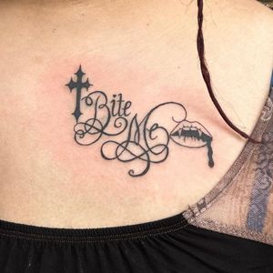 Elegant and mysterious tattoo combining vampire theme, cross, and lips in a small illustrative lettering style by Zanzi La Vey.