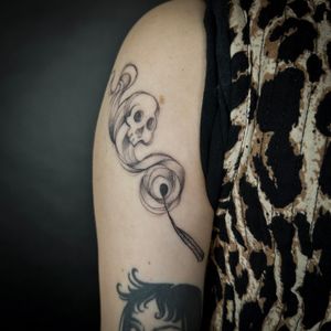 An illustrative black and gray tattoo by Jenny Dubet featuring a skull, death, matchstick, and swirling smoke.