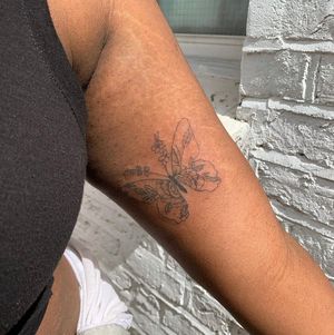Beautiful illustrative tattoo on dark skin by jadeshaw_tattoos, featuring a delicate butterfly and flower design.