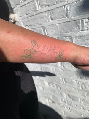 Beautiful fine line flower tattoo in vibrant colors on dark skin by talented artist Jade Shaw. A vibrant and elegant choice for your next tattoo.