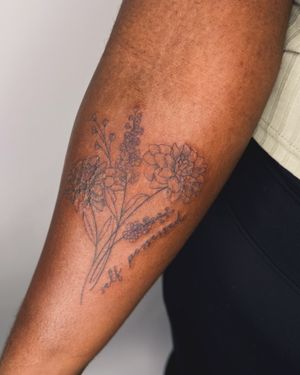 Get inked with a beautifully illustrated flower bouquet on dark skin by jadeshaw_tattoos. Perfect for a small lettering style tattoo.