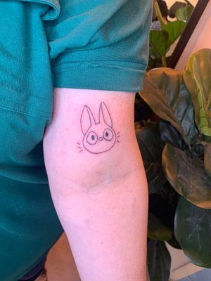 Get a whimsical anime fine line tattoo of Jiji the cat from Studio Ghibli by the talented artist jadeshaw_tattoos.