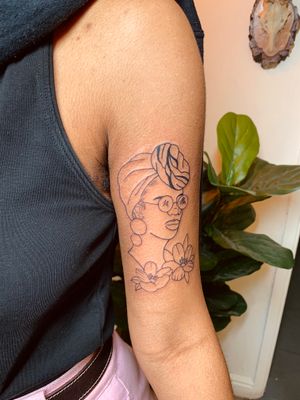 Illustrative tattoo of a beautiful dark skin African woman surrounded by elegant flowers, by jadeshaw_tattoos.