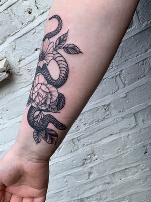 Detailed illustrative tattoo combining a striking snake motif with delicate flowers by jadeshaw_tattoos.