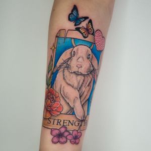 Beautiful tattoo design by Belle Tannahill featuring a rabbit, butterfly, flower, tarot card, and strength symbol.
