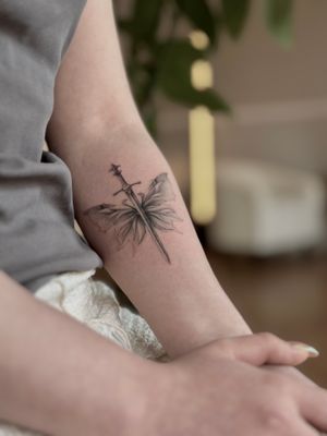Experience the magic of micro realism with this stunning black and gray tattoo featuring a sword, wings, and a fairy by Saka Tattoo.
