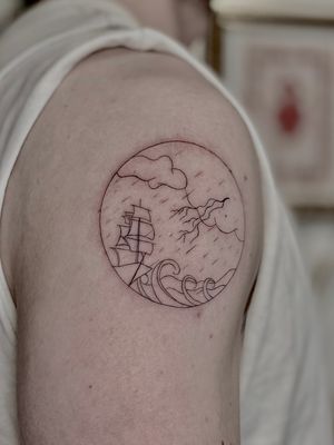 Fine line tattoo by Katerina Nireta featuring a ship battling through a turbulent sea in a decorative frame design.