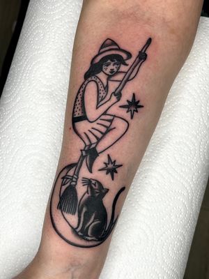 Embrace the magic with this enchanting black and gray traditional tattoo featuring a moon, cat, witch, and broom by Clara Colibri.