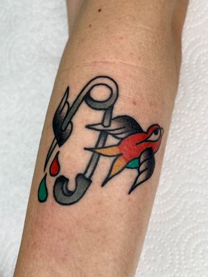 A stunning traditional tattoo featuring a swallow, clothes pin, and safety pin, beautifully executed by Clara Colibri.