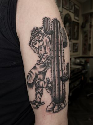 Capture the spirit of the wild west with this black and gray traditional tattoo of a cowboy and cactus by Barney Coles.