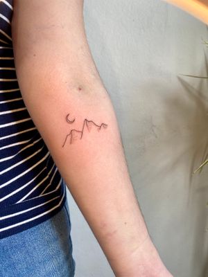 Get a unique fine line, hand-poke tattoo of a stunning moonlit mountain peak by Charlotte Pokes. Perfect for nature lovers and adventurers.