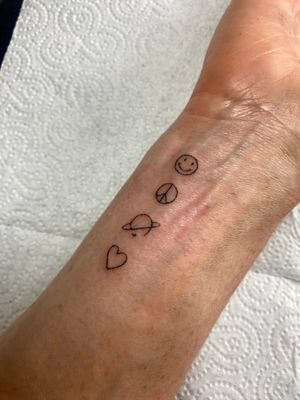 Capture the essence of peace and love with this fine line hand poke tattoo featuring a heart, peace symbols, and a smiley face by Charlotte Pokes.