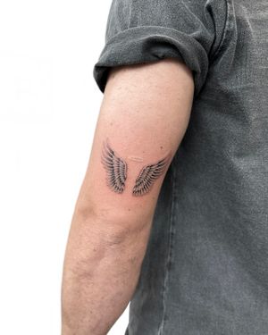 Beautiful black and gray tattoo of angel wings and a ring, created by Alex Lloyd.