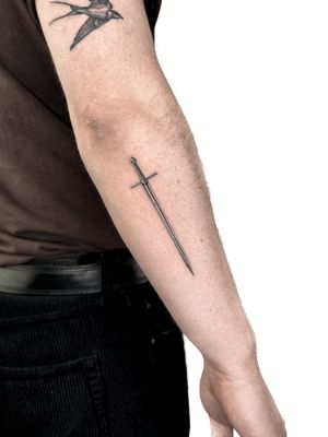 Stunning black and gray sword tattoo by the talented artist Alex Lloyd, showcasing fine details and realistic shading.