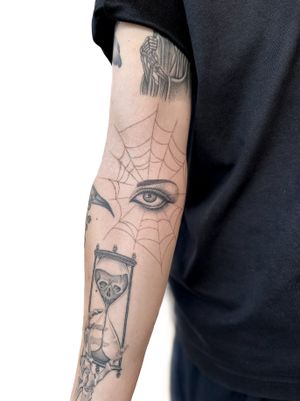 Alex Lloyd's black & gray fine line tattoo showcases a micro-realism eye trapped in an illustrative spiderweb design.
