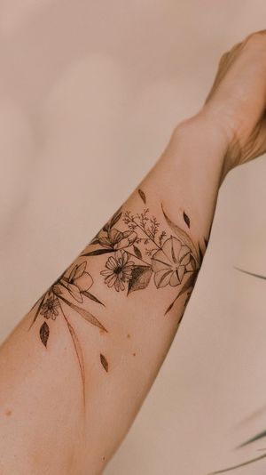 fine line wildflowers and birth flowers wrap around the forearm with the names of her children