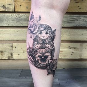 Black and grey, blackwork, illustrative fineline tattoo of a Russian doll and flowers