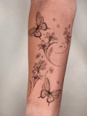 Fine line black and gray tattoo by Alex Caldeira featuring a delicate butterfly and flower with intricate sparkle details.