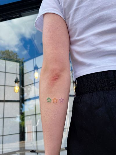 A delicate fine line hand-poked tattoo of a colorful star, created by artist Laura.