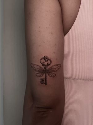 Black and gray dotwork tattoo of micro realistic fairy wings with a key, by artist Lauren.