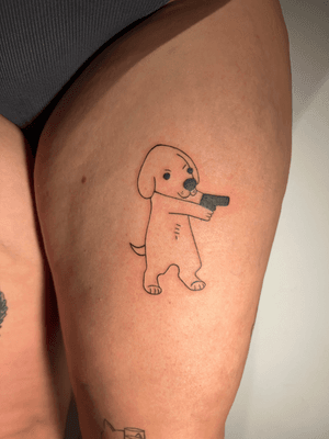 Fine line tattoo by Inna featuring a cute puppy and an intricate gun doodle, highlighting the contrast between innocence and danger.