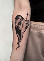 Black and grey surreal realism tattoo featuring a feminine face emerging from a melting heart silhouette.