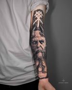 Mimir & Yggdrasil – Norse Mythology Forearm Tattoo A black and grey realism tattoo inspired by Norse mythology, featuring Mimir, the wise guardian of knowledge, alongside the Yggdrasil tree of life. Symbolizing wisdom and eternity, this detailed forearm piece combines depth and symbolism. Tattoo by London artist Roudolf Dimov.