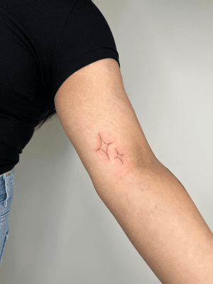 A delicate fine line tattoo of a sparkling star by Emma InkBaby.