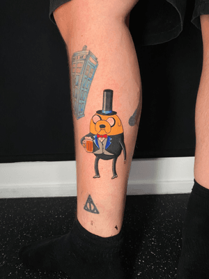 An anime-style tattoo featuring Jake from Adventure Time wearing a top hat, showcasing his gentlemanly side. By artist Marie Terry.