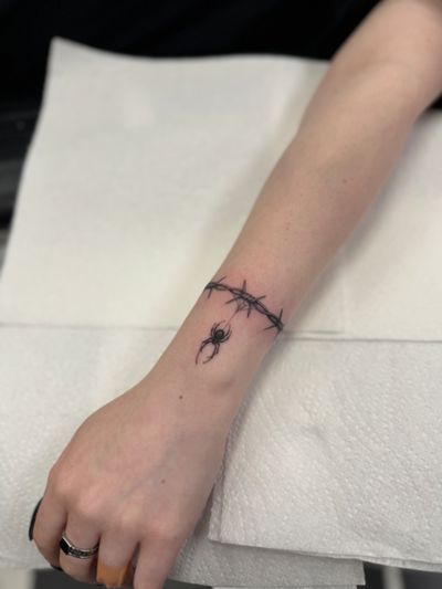 Get a stunning black and gray micro realism tattoo by Dani Mawby featuring a detailed spider crawling through barbed wire.