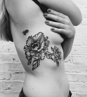 Elegant tattoo on the ribs featuring a bee and flower motif, expertly executed in fine line floral style by Sandro Secchin.