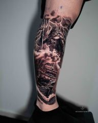 Black and grey realism calf tattoo featuring Poseidon, the Greek god of the sea, holding his trident above a sailing ship battling powerful ocean waves. Dramatic lightning, storm clouds and detailed shading create a dynamic Greek mythology composition. Custom tattoo by Roudolf Dimov, London, UK.