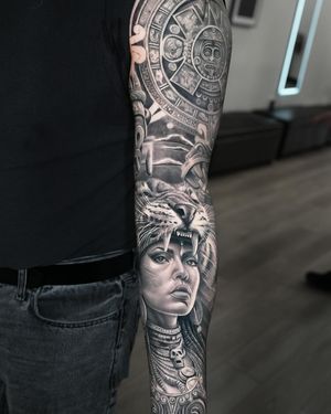 A realistic black and gray tattoo featuring a fierce huntress with native Aztec, Inca, and Mayan elements, including a leopard companion. By tattoo artist Ember.