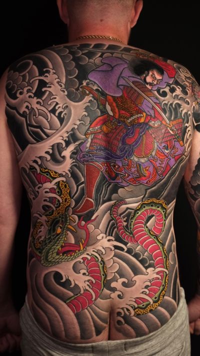 A majestic samurai warrior battling a fierce snake amidst traditional Japanese waves, expertly tattooed by Martin Kirke.