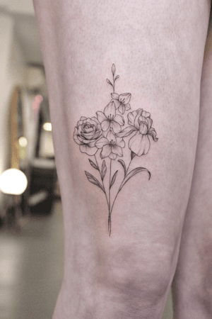 A black and gray tattoo by Ayala featuring a delicate bouquet of fine line floral designs.