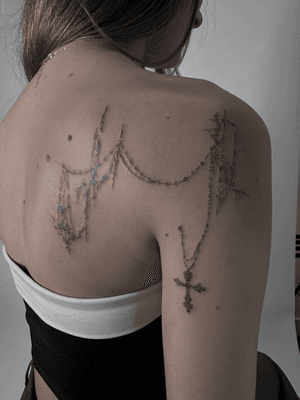 A meticulously detailed tattoo of a cross intertwined with a rosary, designed by artist Oliver Soames in a fine line neotribal style.