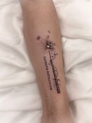 Small lettering and illustrative style tattoo combining a flower, Harry Potter theme, and magic wand by artist Alex Caldeira.