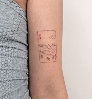 A fine line illustrative tattoo by Ally.ink featuring a serene ocean sunset scene with a playing card motif, ace and king of diamonds.