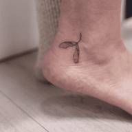 Tiny small dainty delicate and discrete ankle tattoo of a sycamore seed, an autumn fall themed fineline tattoo